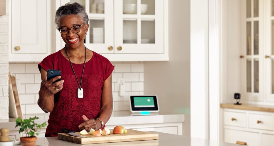 Woman in kitchen using her phone and wearing a Vivint emergency pendant