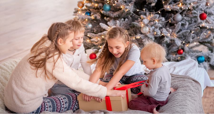 Siblings opening a present beside a Christmas tree.